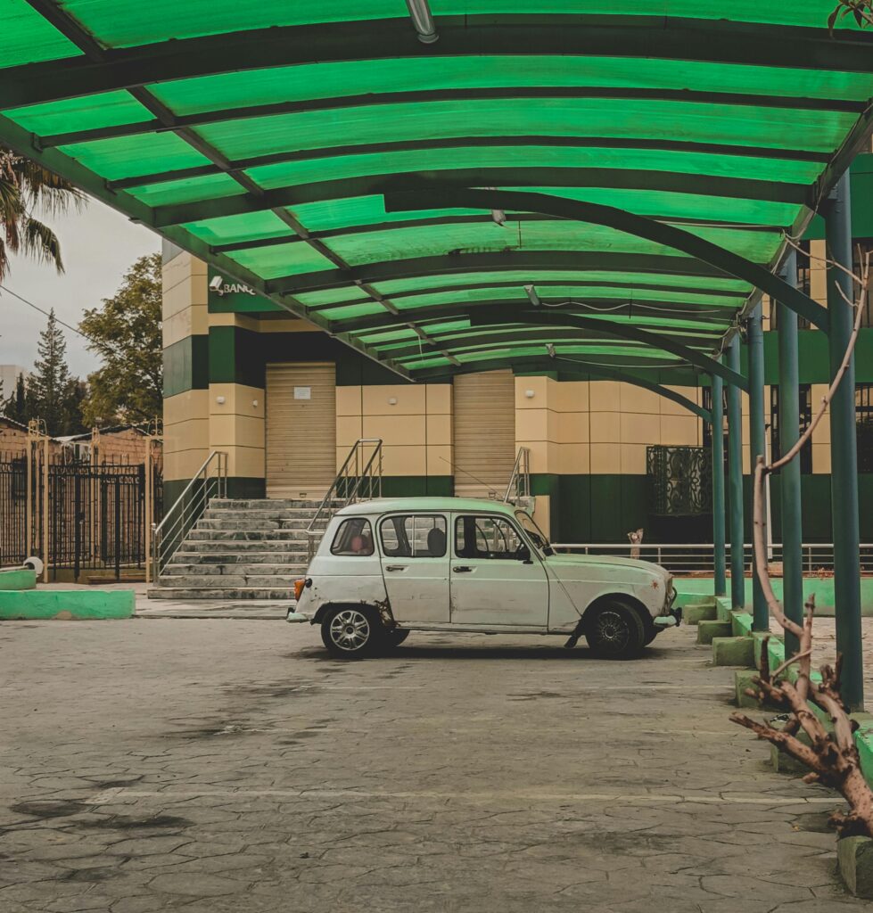 Classic car parked under a modern green roof structure, outdoors.